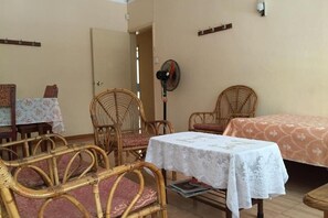 A room with wicker furniture, a bed with a patterned bedspread, a table with a lace tablecloth, and a standing fan. - Pereybere Beach Apartments: Superior Apartment (Pereybere)