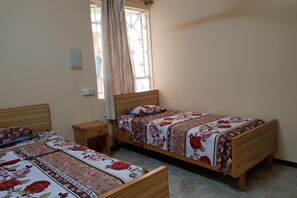 A bedroom with two wooden beds, each with floral bedding, a small bedside table, a nightstand, and a window with curtains. - Pereybere Beach Apartments: Superior Apartment (Pereybere)