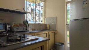 A kitchen with a microwave, stove, sink, and a window with decorative iron bars. - Pereybere Beach Apartments: Superior Apartment (Pereybere)