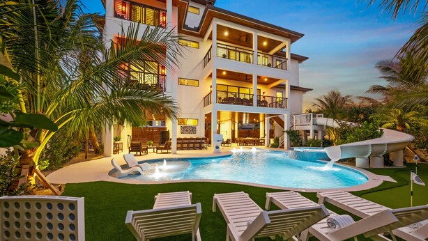Um edifício moderno de dois andares com piscina, área de estar externa e vegetação exuberante.