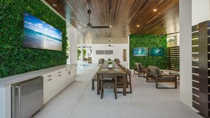 Cozinha moderna com uma ilha grande, área de jantar com uma mesa comprida e cadeiras, e sala de estar com TV e decoração de parede verde.