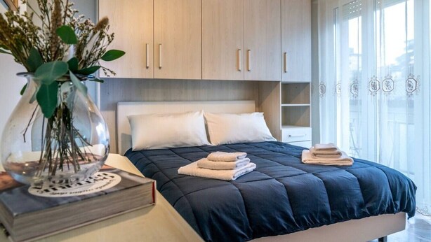 A bedroom with a bed, a bedside table with a book and a vase, and a window with curtains.