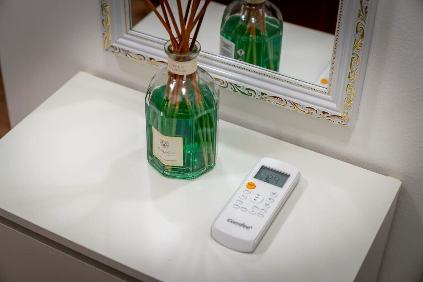A white bathroom vanity with a green bottle and a white electronic device on it.