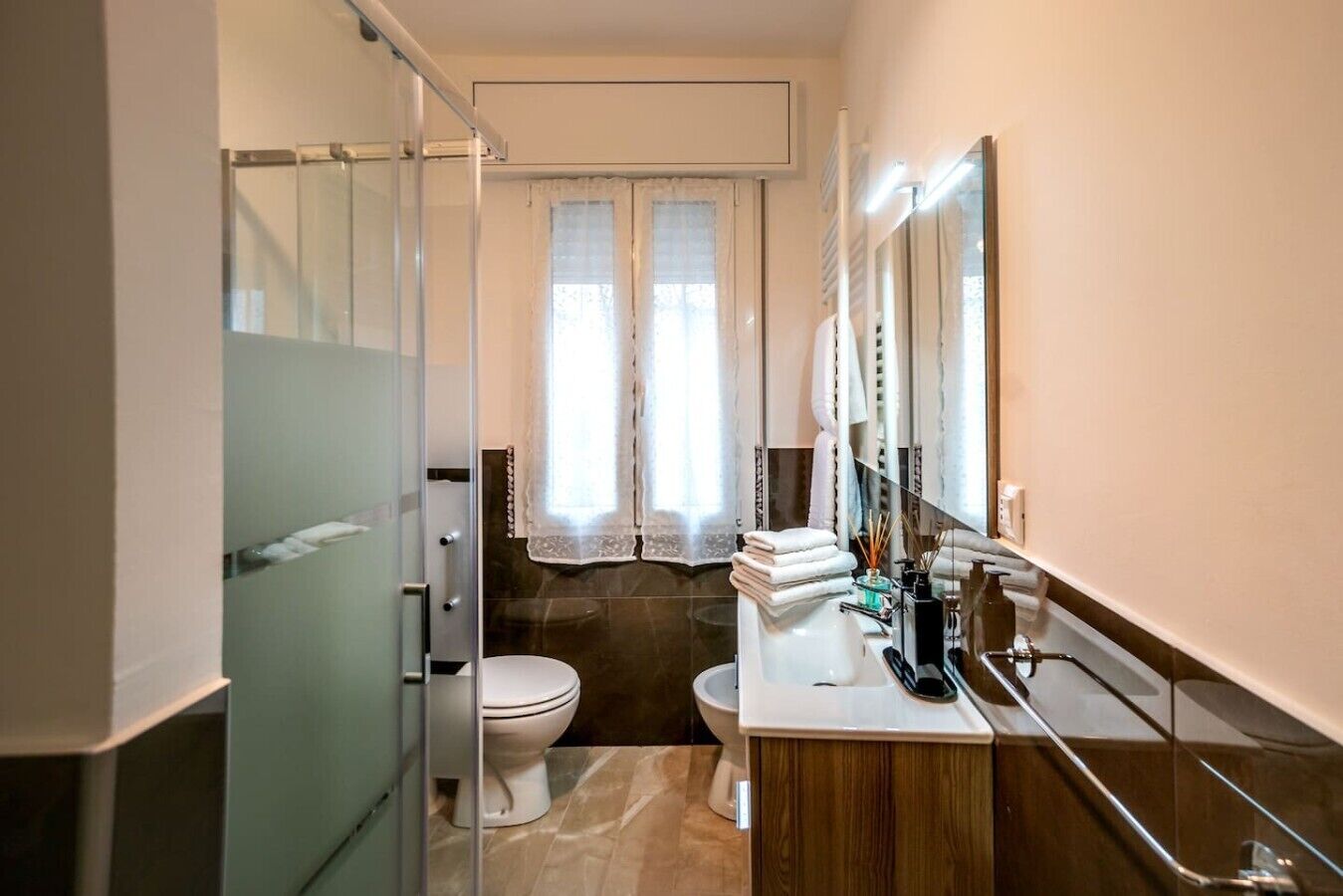 Ein Badezimmer mit Duschkabine, Toilette, Waschbecken mit Spiegel und einem Fenster mit Vorhängen.