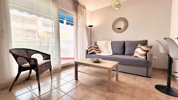Una sala de estar con sofá, una silla de mimbre, una mesita de centro y una lámpara de pie.