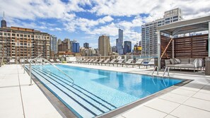 Ein Pool auf dem Dach mit Liegestühlen und einer Stadtansicht im Hintergrund.