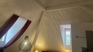 Et værelse med skråvægge, en hængende lampe, et vindue med gardiner og en dør.