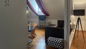 Et værelse med skråvæg, spiseplads med bord og stole, en sort sofa, en gulvlampe og en radiator.