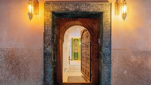 An ornate wooden door with intricate carvings and a number '10' sign above it, leading into a room with a patterned floor and a green carpet. - Luxury Taj Riad Zitoune (Marrakech)