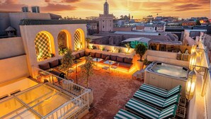 A rooftop terrace with a hot tub, outdoor seating, and a view of the cityscape at sunset. - Luxury Taj Riad Zitoune (Marrakech)