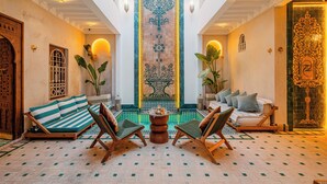 A spacious lounge area with a central fountain, cushioned seating, and a decorative wall with intricate patterns. - Luxury Taj Riad Zitoune (Marrakech)