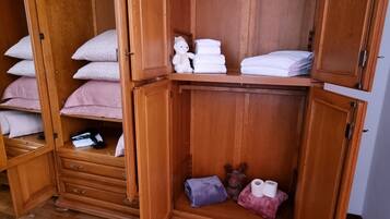 A wooden wardrobe with multiple shelves, some containing folded towels and pillows, and a small shelf with a plush toy and a rolled-up towel.
