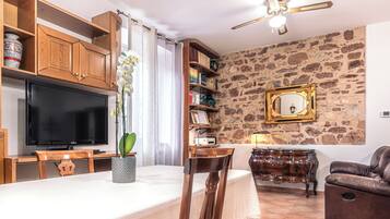 A living room with a television, wooden cabinets, a stone wall, a sofa, and a dining area with chairs and a table.