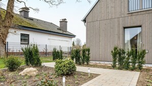 Une maison moderne dotée d’un jardin aménagé avec une allée pavée et une cour clôturée où diverses plantes sont cultivées.