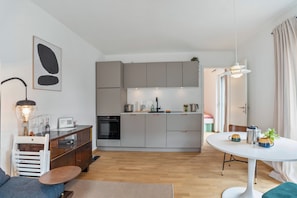 Une cuisine moderne avec des meubles gris, un four encastré et un coin repas comprenant une table et des chaises blanches.