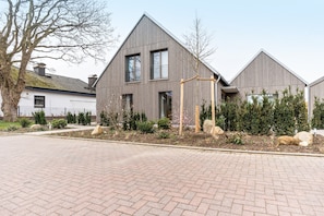 Une maison moderne avec un toit en pente, de grandes fenêtres et une allée pavée.
