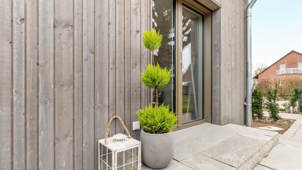 Un bâtiment moderne avec un revêtement en bois, une plante en pot et une lanterne sur le porche.