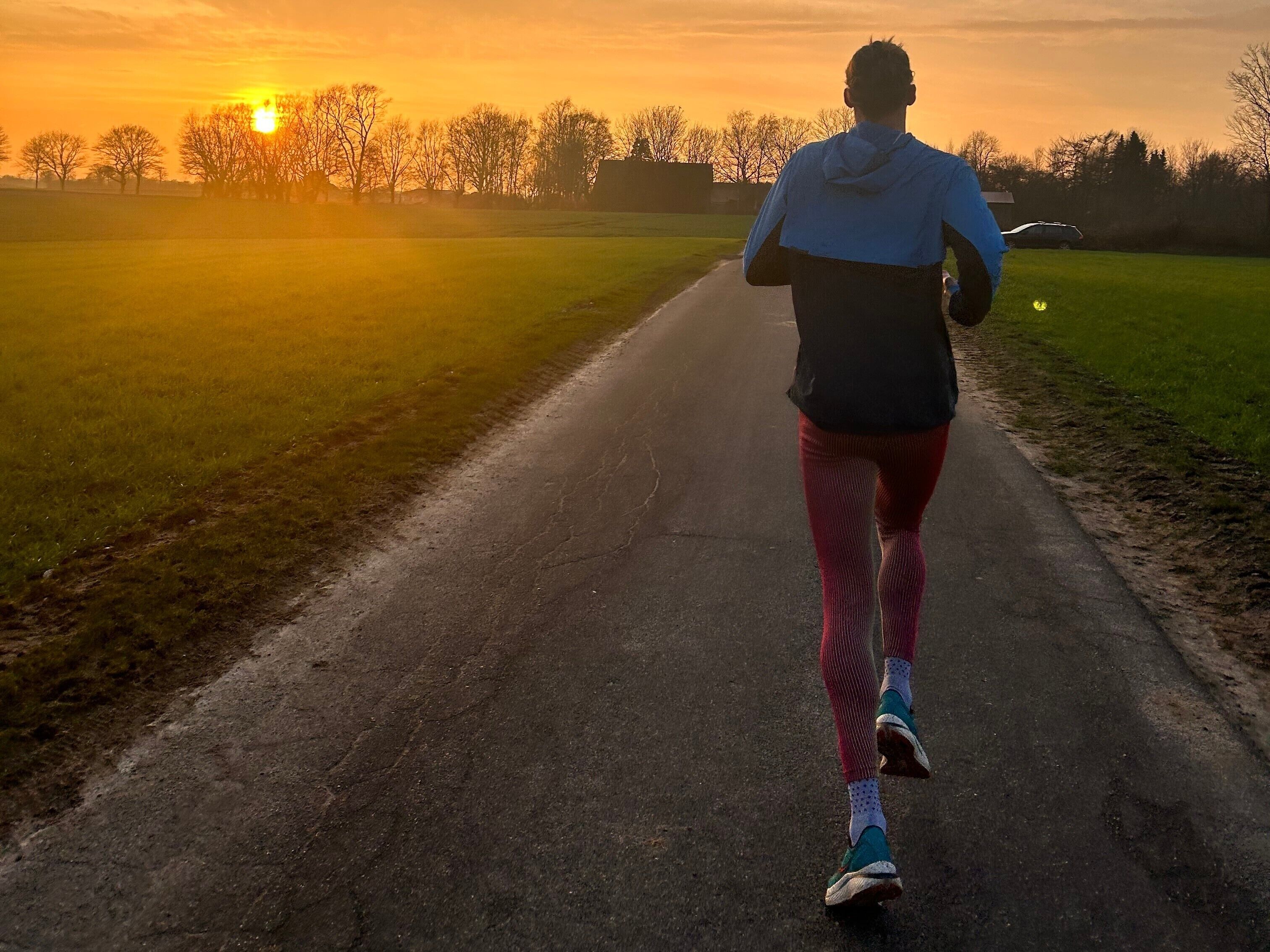 A person running on a paved path with a sunset in the background.