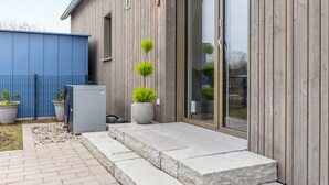 Un bâtiment moderne avec une façade en bois, une clôture bleue et une terrasse pavée avec des marches menant à une porte.