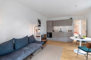 Un salon moderne comprenant un canapé, une table à manger avec des chaises, un coin cuisine et un escalier menant à un autre niveau.