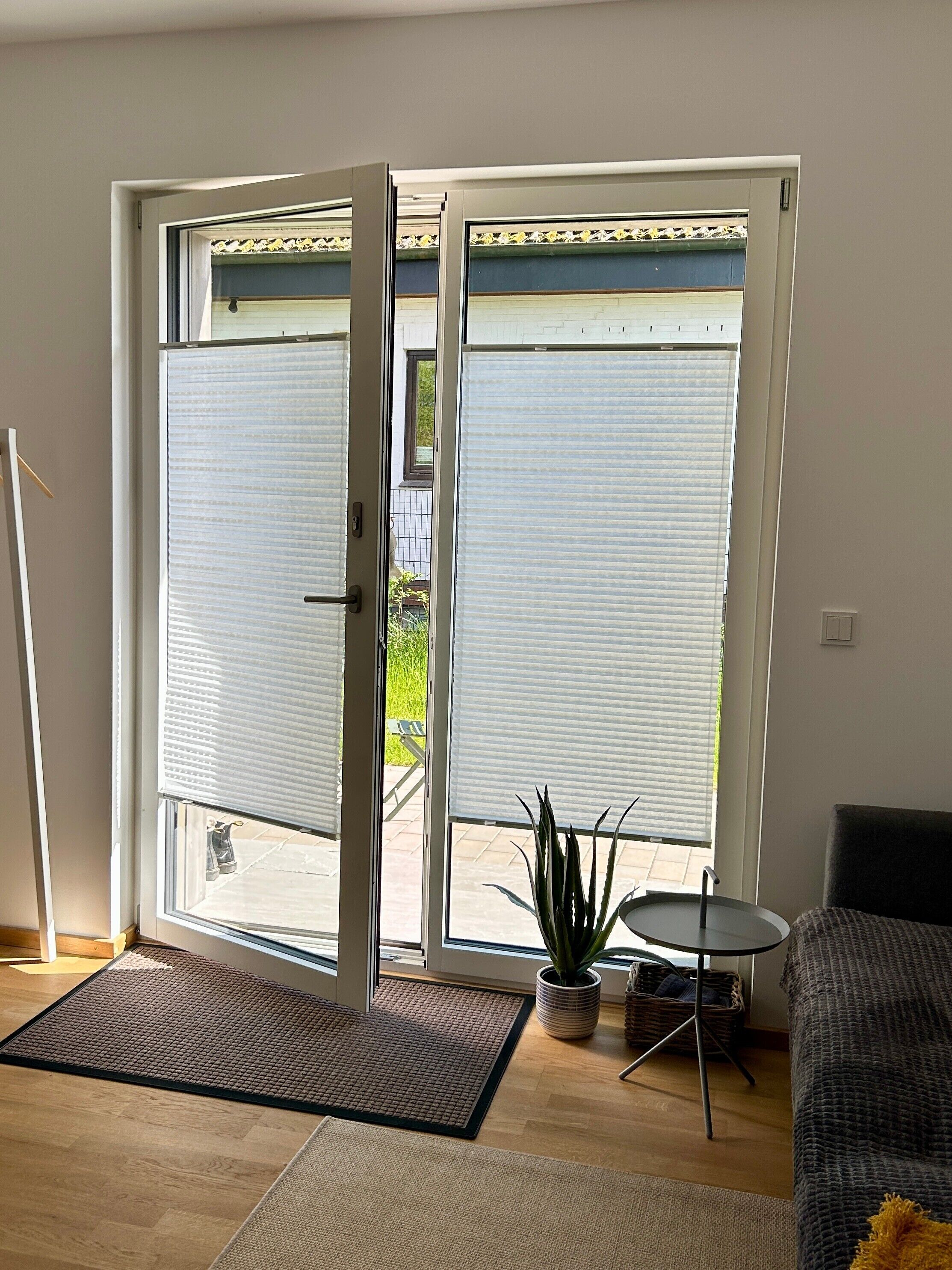 Ein Zimmer mit einer Glasschiebetür, die auf eine Terrasse führt, einem kleinen runden Tisch mit einer Pflanze und einem Sofa.