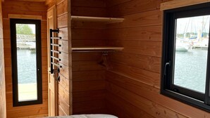 Ein Zimmer in einer Holzhütte mit einem Bett, einem Fenster mit Blick auf Boote und einer Tür, die nach draußen führt.