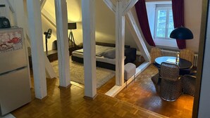 Quarto de loft aconchegante com uma cama, uma mesinha, cadeiras de vime e uma janela com cortinas.