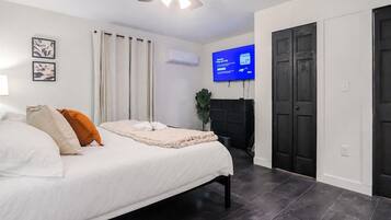 A bedroom with a bed, curtains, a TV, a dresser, and a door.