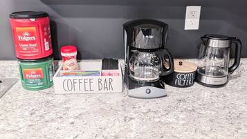Una encimera de cocina con equipo para preparar café, incluyendo una cafetera, filtros y latas de café Folgers.