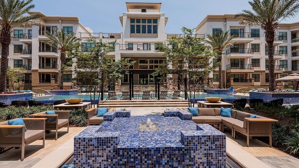 A hotel with a pool area featuring tiled flooring, lounge chairs, and a central fountain. - Landing | Beautiful 2BD, Clubhouse, Rooftop Lounge (San Antonio)