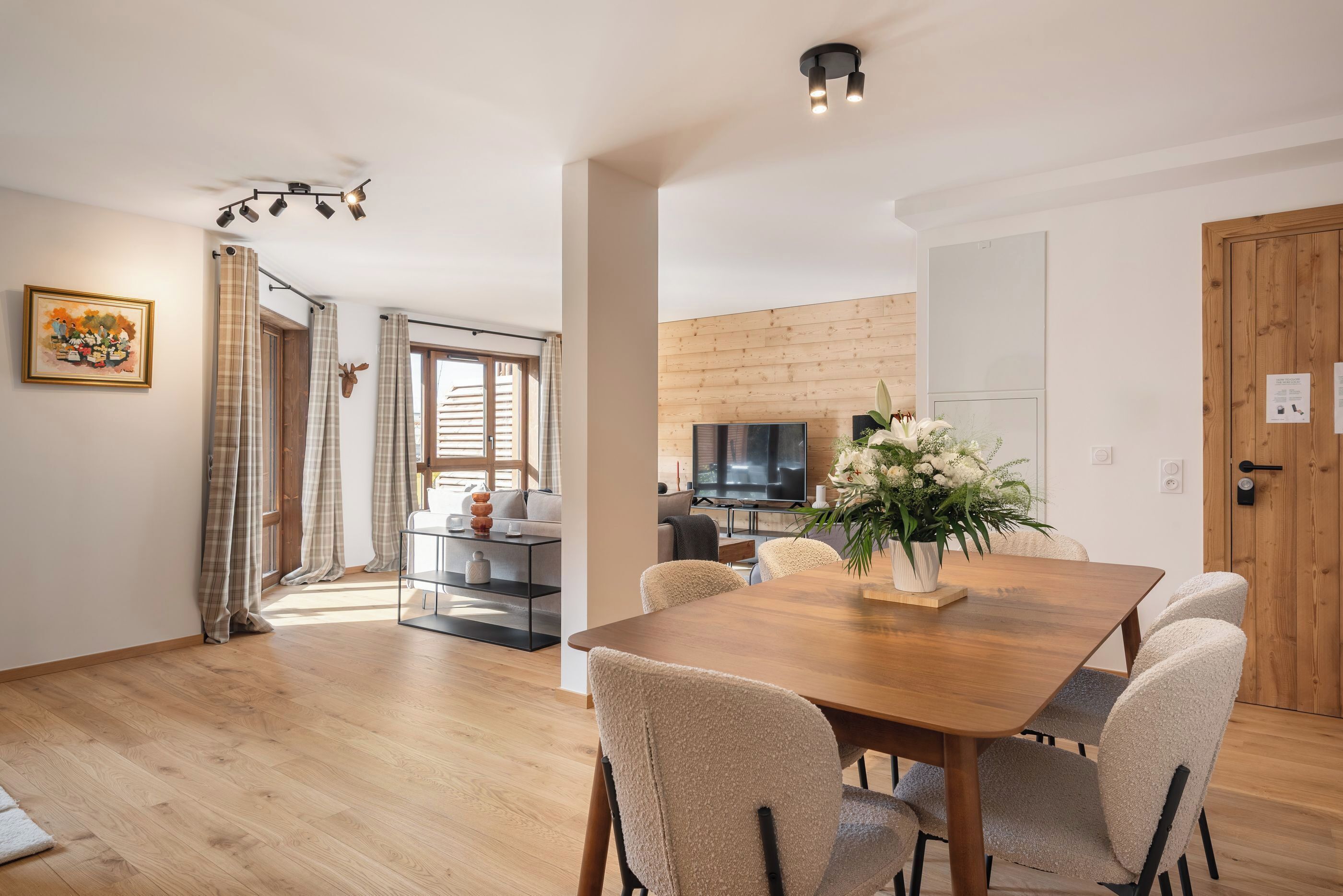 Ein modernes Wohnzimmer mit einem Holzespeisetisch, beigen Stühlen, einem Fernseher und einer Holzverkleidung.