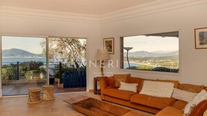A spacious living room with a large sofa, a coffee table, and a view of a coastal landscape through large windows.
