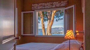 A bedroom with a bed, a window with an open view of trees and mountains, and a lamp on the side table. - Villa AMBRA - 6 bedrooms, panoramic sea view, swimming pool (ALBITRECCIA)