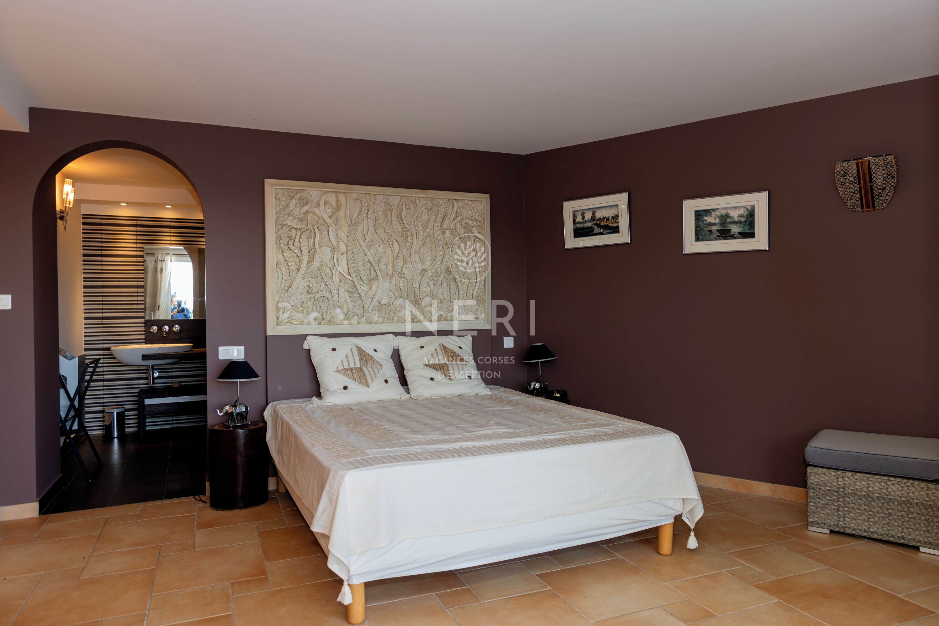 A bedroom with a large bed, a vanity with a mirror, and a dining area with a table and chairs.