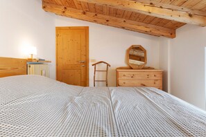 A bedroom with a wooden ceiling, a bed with a checkered bedspread, a wooden dresser, a mirror, and a wooden door.