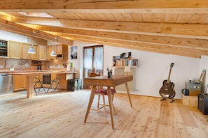 A kitchen with wooden beams, a dining area with a table and chairs, and a guitar against the wall.