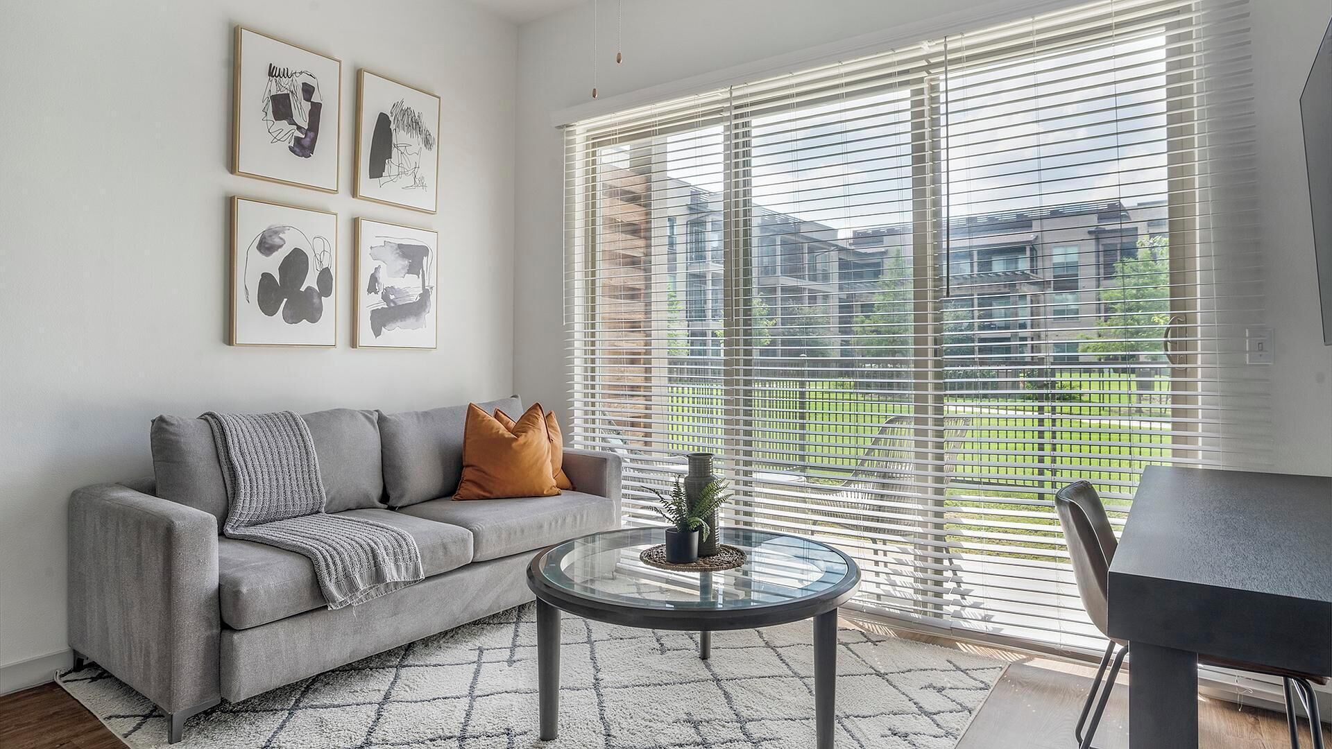 A modern living room with a grey sofa, a glass coffee table, and a view through large windows.
