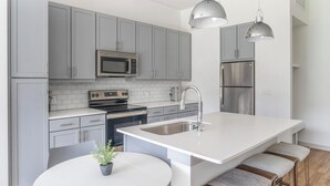 Une cuisine moderne avec des meubles gris, des appareils en acier inoxydable, un îlot central blanc doté de tabourets de bar et un éclairage suspendu.