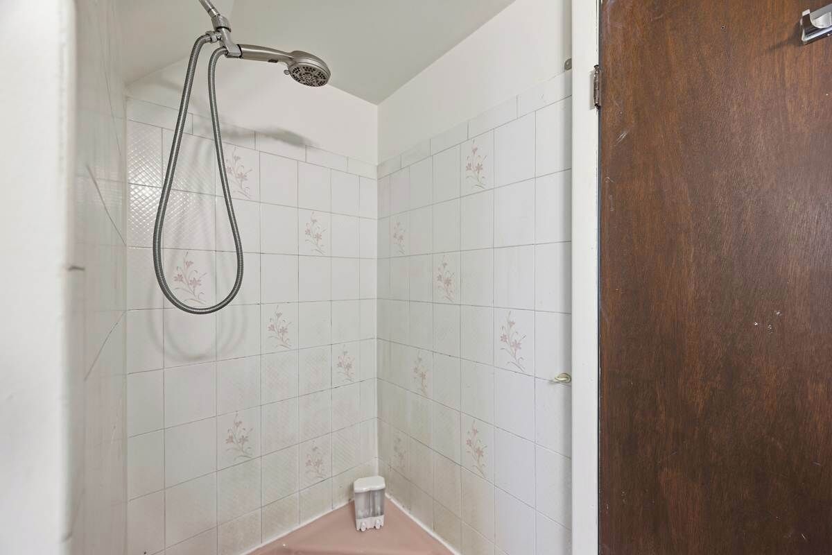 A bathroom with white tiles, a shower, and a wooden door.