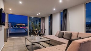A modern living room with a sofa, a coffee table, and a dining area with chairs and a plant. - Acropolis Magical View Suite, Metro Kerameikos (Athens)