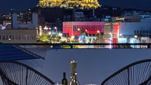 A table set with wine glasses and bottles, overlooking a cityscape with illuminated buildings and a view of the Acropolis. - Acropolis Magical View Suite, Metro Kerameikos (Athens)