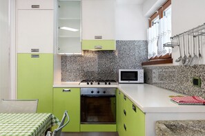 Une cuisine de taille réduite équipée d’une cuisinière à gaz, d’un four, d’un four à micro-ondes et d’une fenêtre avec des rideaux.