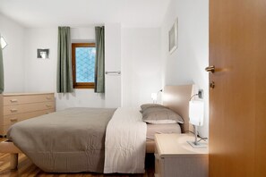 Une chambre à coucher avec un lit, une table de chevet, une lampe et une fenêtre avec des rideaux.