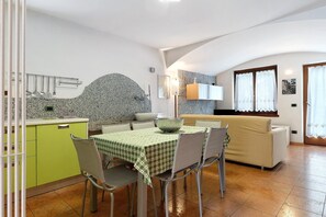 Un coin repas avec une table dressée pour deux personnes, une cuisine dotée de plans de travail en granit et un canapé en arrière-plan.