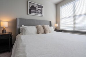 A neatly made bed with a grey headboard, two bedside lamps, and a framed picture above the bed. - Landing | Chic 2BD, Courtyard, Clubhouse (San Antonio)
