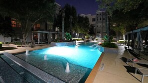Un espace piscine nocturne doté de plusieurs éléments aquatiques, de chaises longues et d’un éclairage soigné.