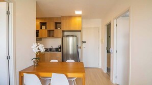 Una cocina compacta con armarios de madera, un refrigerador de acero inoxidable y un comedor con mesa de madera y sillas blancas.