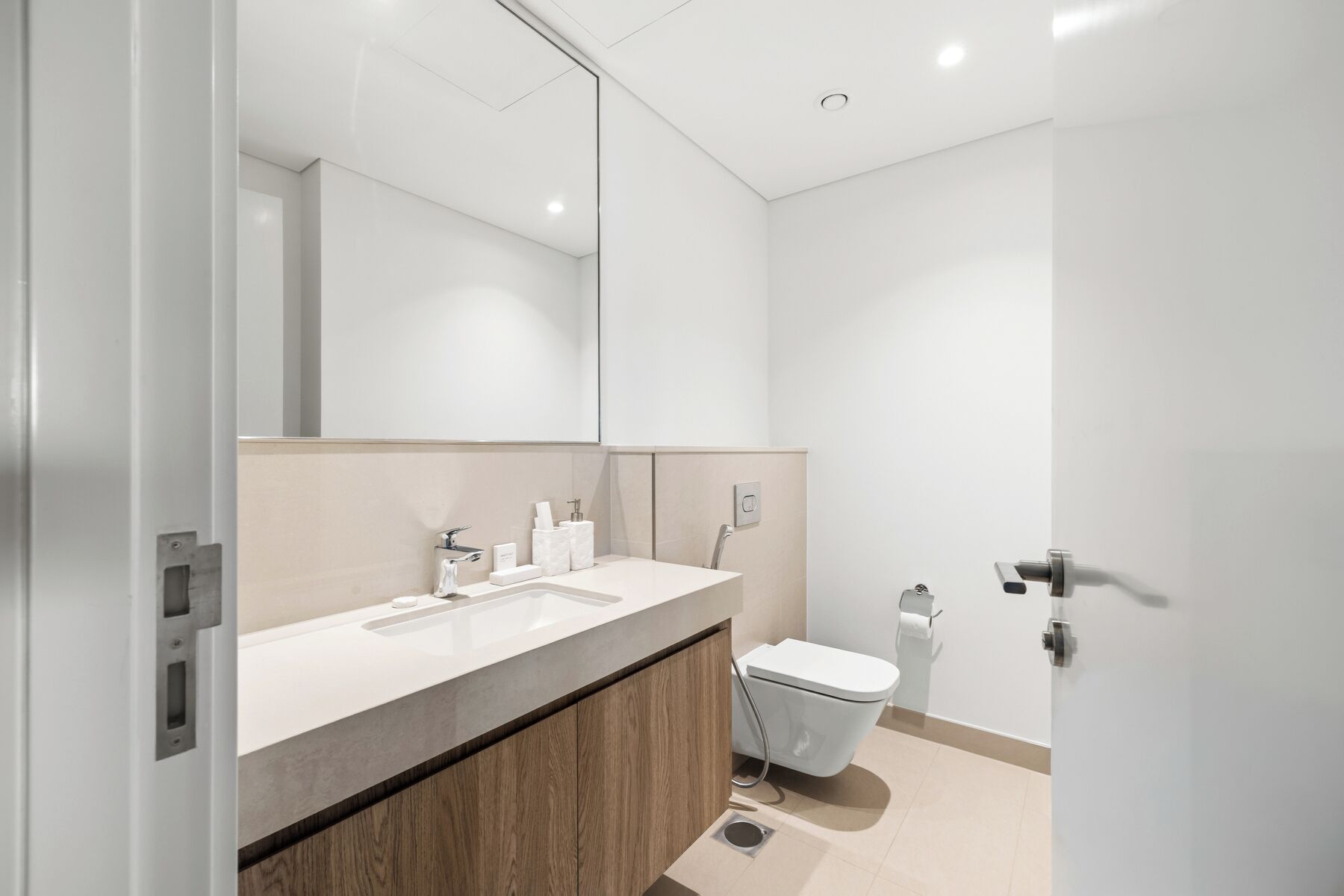 A modern bathroom with a large mirror, two sinks, a toilet, and a shower area.