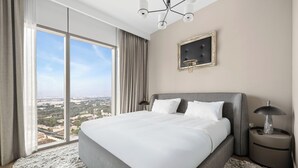 Moderni hotellihuone, jossa on suuri sänky, näköala kaupunkiin ja koristeellinen kattokruunu.