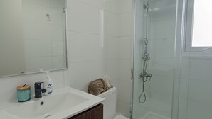 Un baño moderno con un lavabo blanco, un espejo, un inodoro y una ducha con mampara de vidrio.